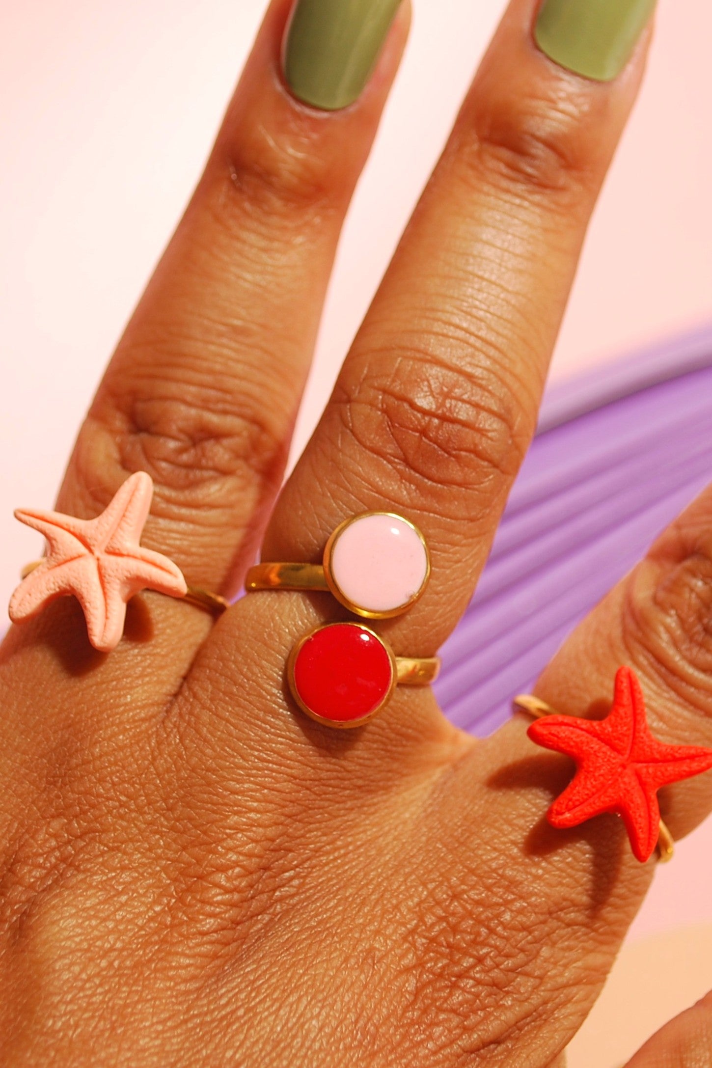 Hand mit Santoclay Ringen – Seesternringe & runde Ringe in Rot, Pink & Gold, handgefertigt aus Polymer Clay & Edelstahl