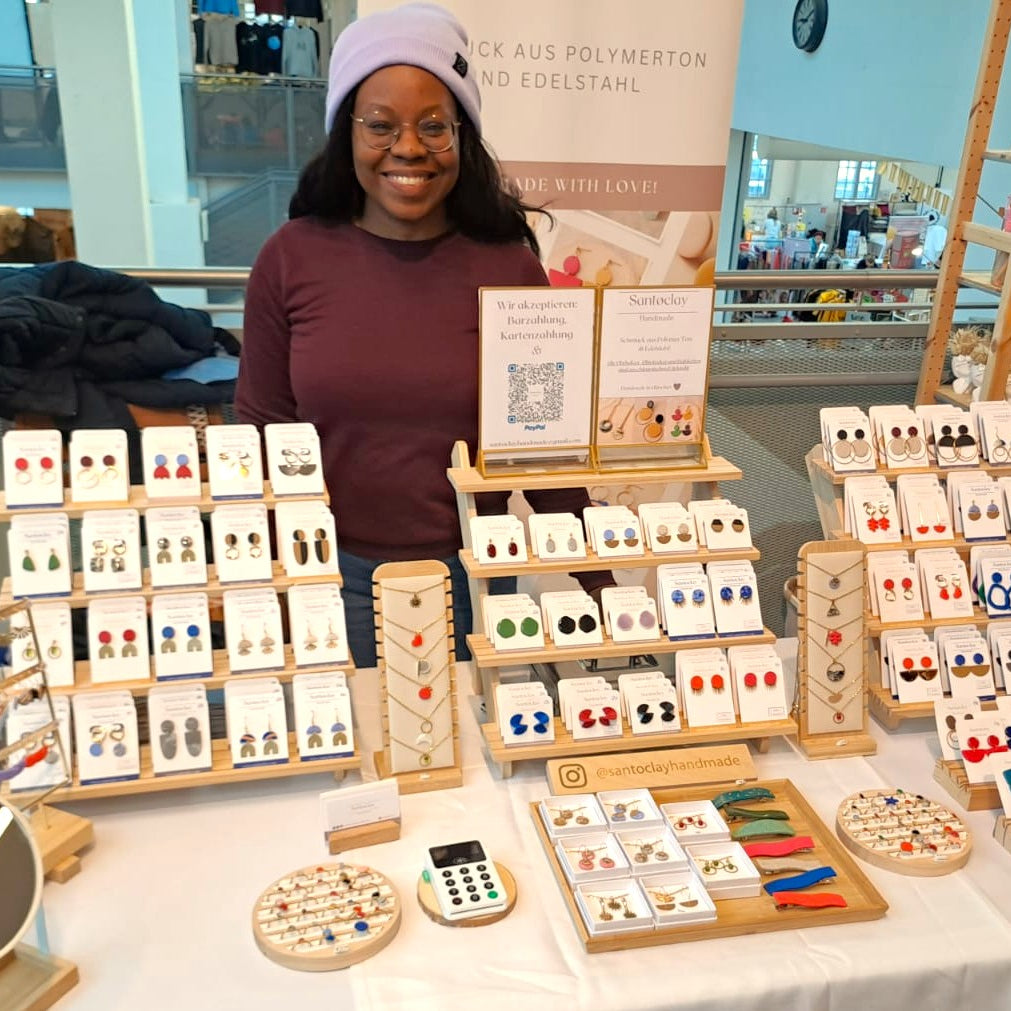 Flávia Troppmann, junge Schmuckdesignerin präsentiert handgemachte Ohrringe, Ketten und Accessoires von Santoclay Handmade an einem liebevoll dekorierten Marktstand – ideal für moderne, farbenfrohe Schmuckliebhaber.