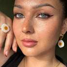 Frau trägt handgemachten Schmuck aus der Eggstasy Kollektion – weiße und gelbe Ohrringe, Ring und Halskette von Santoclay Handmade, handgemacht in München.